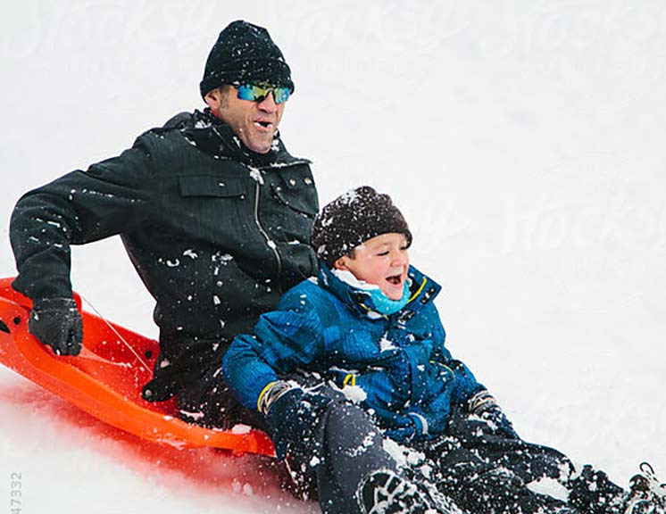 Dad and son on an orange sled while its snowing