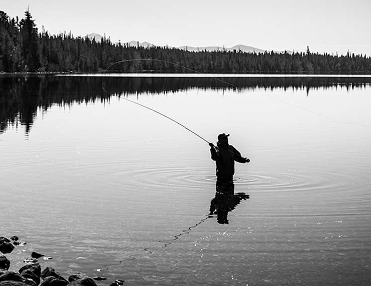 Fisherman fly fishing waist deep in mountain lake