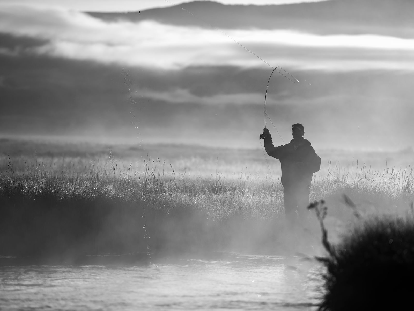 Black and white photo of someone fishing in the fog