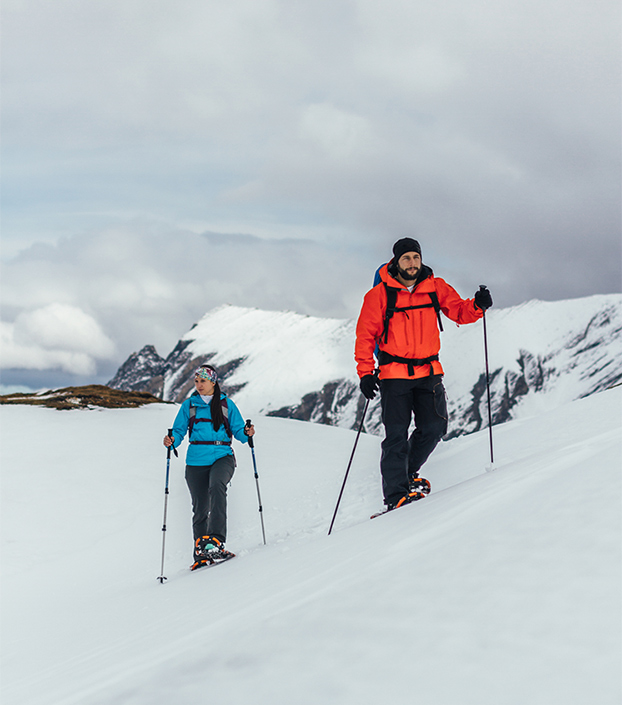 Two people with hiking poles snowshoeing on a mountain peak