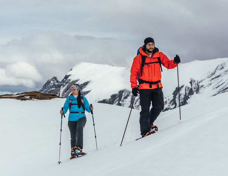Two people snowshoeing on top of a mountain peak