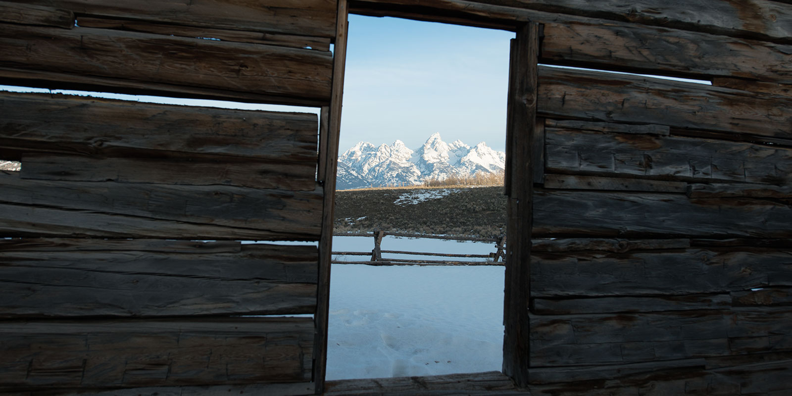 View from an old wooden barn window frame looking at snow capped Grand Tetons