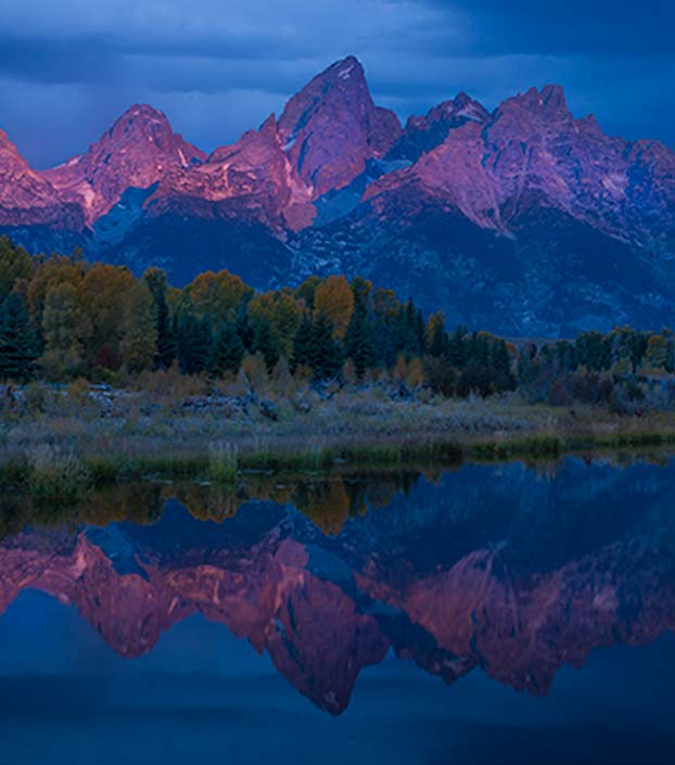 Grand Teton National Park sun shining on mountain peaks and reflected in the lake surrounded by trees