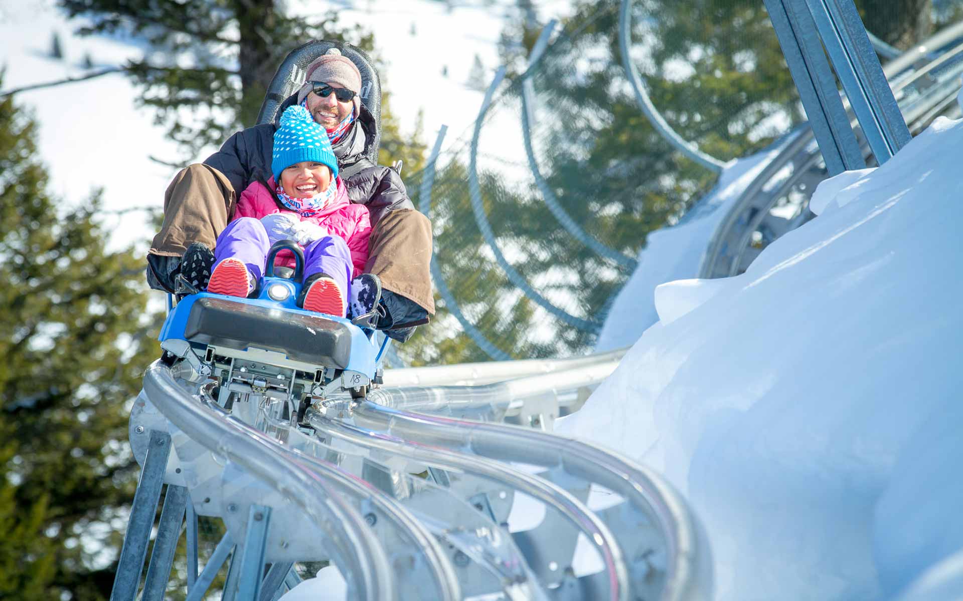 Dad and daughter going down Alpine Slide in winter at Snow King Mountain