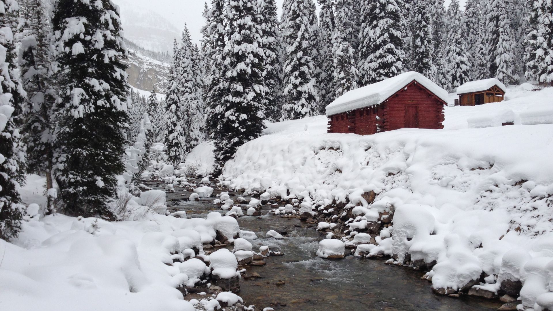 Jackson Hole winter scene with mountain stream, snow covered pine tress and wooden buildings with snow covered roofs