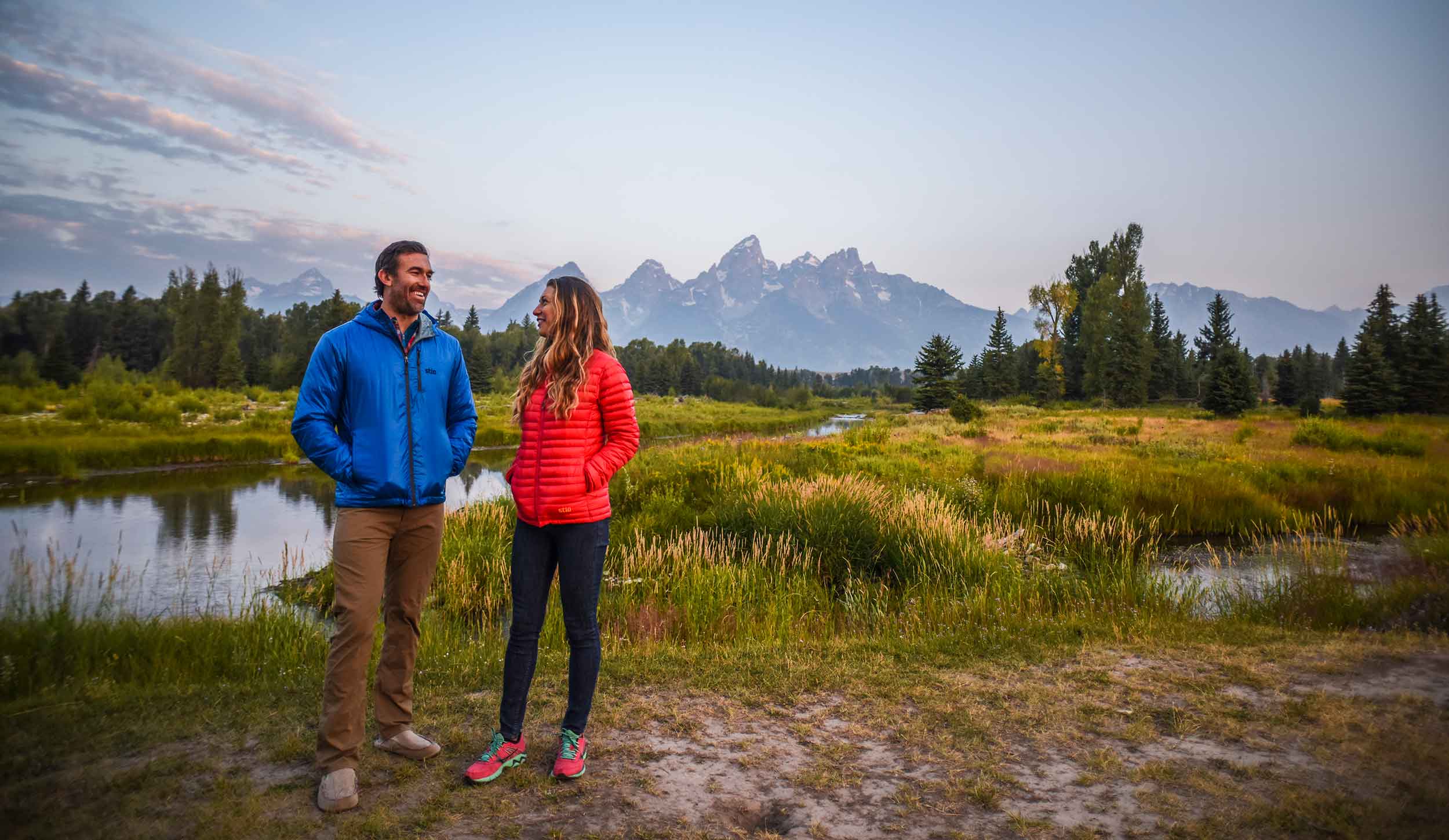 Couple standing in meadow along river with Grand Tetons in background
