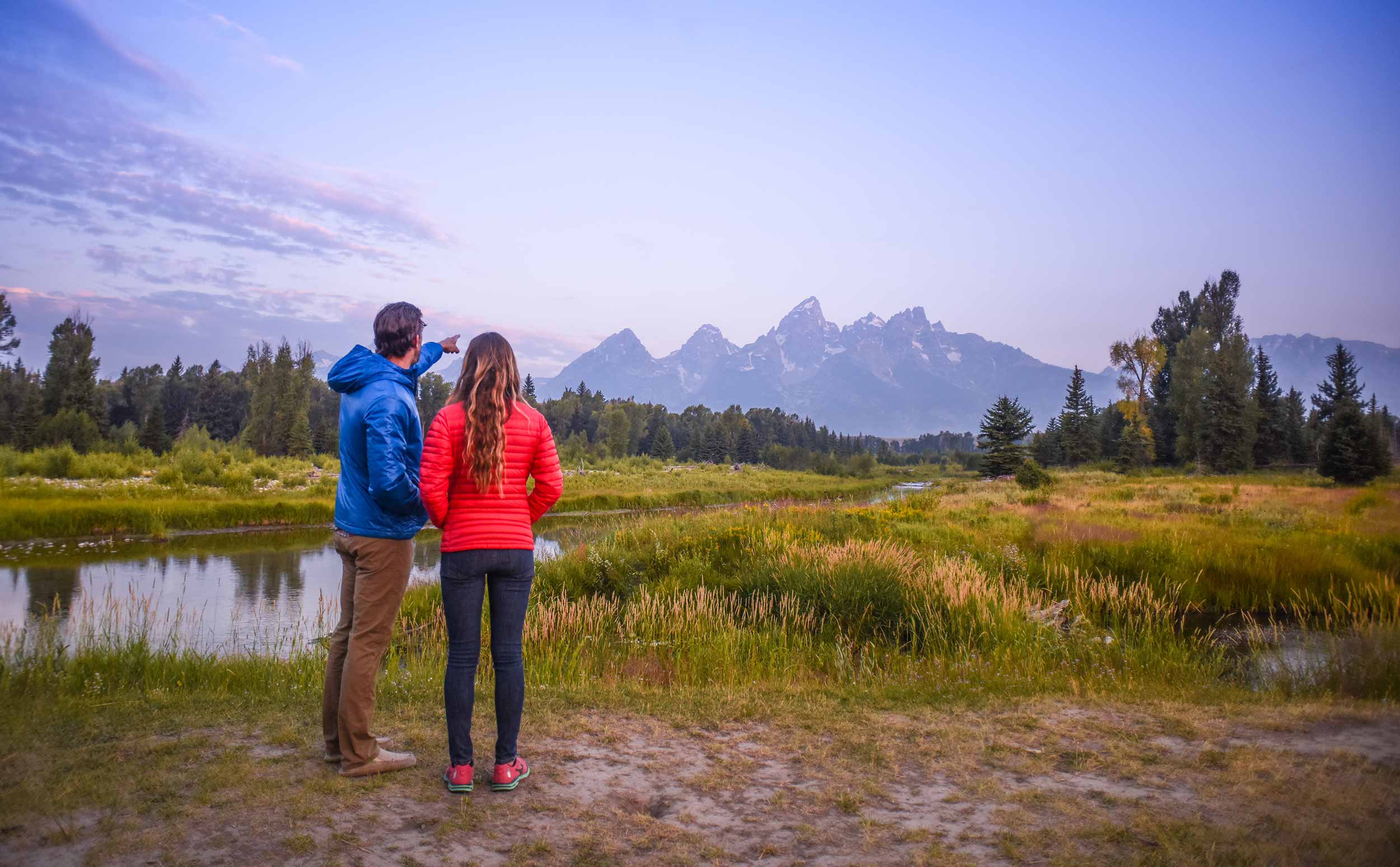 Couple along river pointing to Grand Tetons
