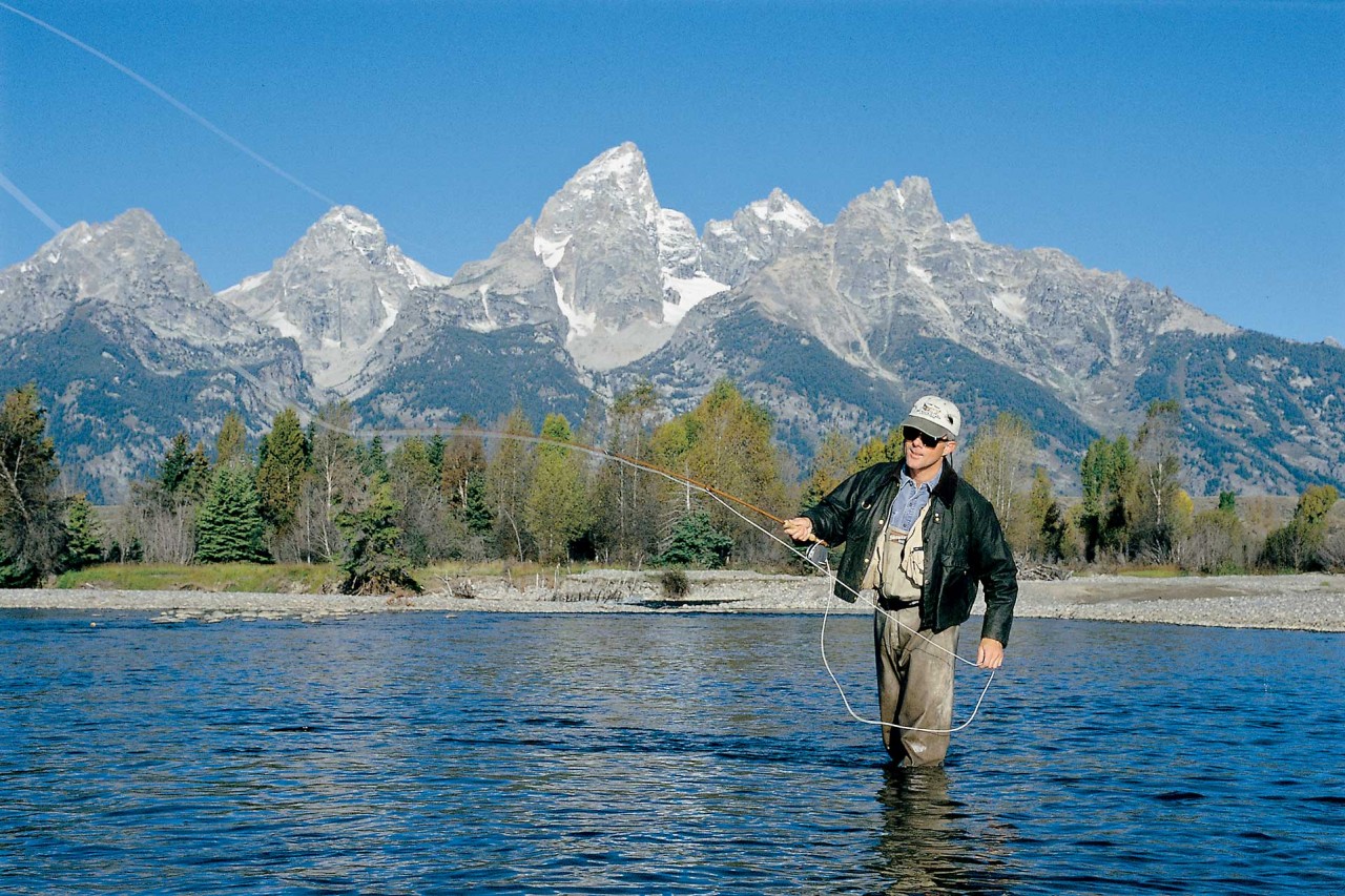 Fly fishing in Jackson Hole in mountain lake with Grand Tetons in background
