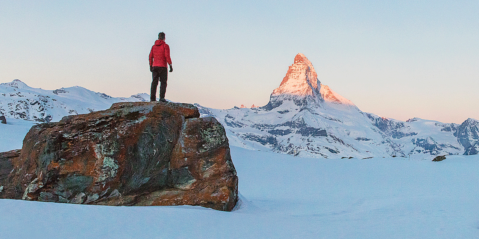 Man on mountain boulder in winter looking at mountain peak at sunrise