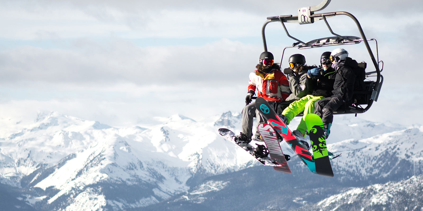 Four snowboarders on ski lift chair with view of snow capped mountains